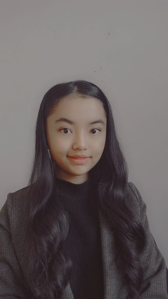 Young teen Central Asian girl with long dark hair and brown eyes wearing a gray jacket over a black sweater. 