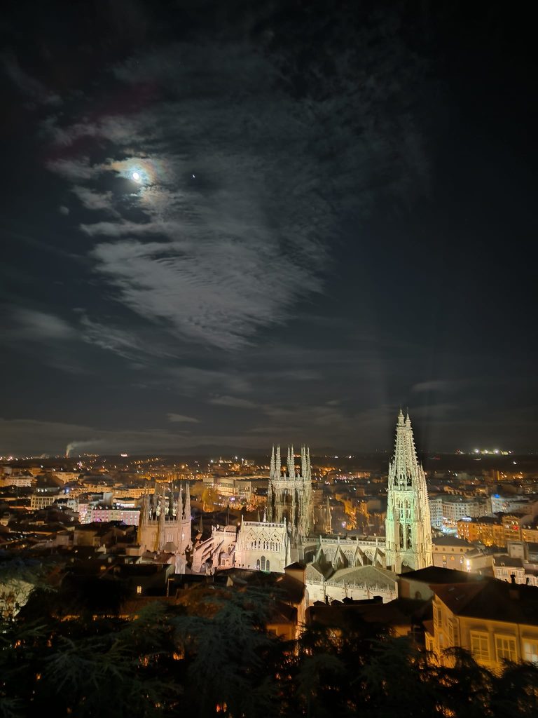 Moonlit, partly cloudy night. Historical city with cathedral spires and other buildings lit up at night. 