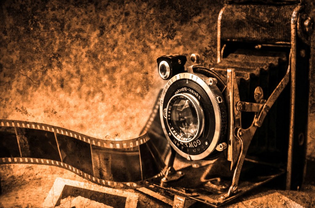 Old film camera with handles and black and white film coming out of it. Sepia photograph. 