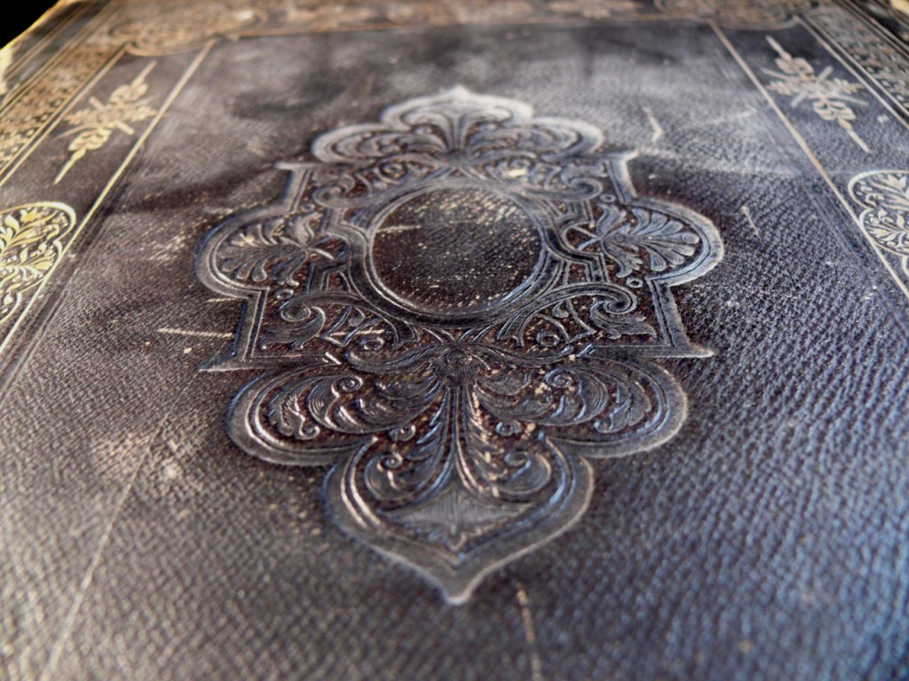 Filigree metal silver seal on a old faded cover of a book with a border and a leather design.