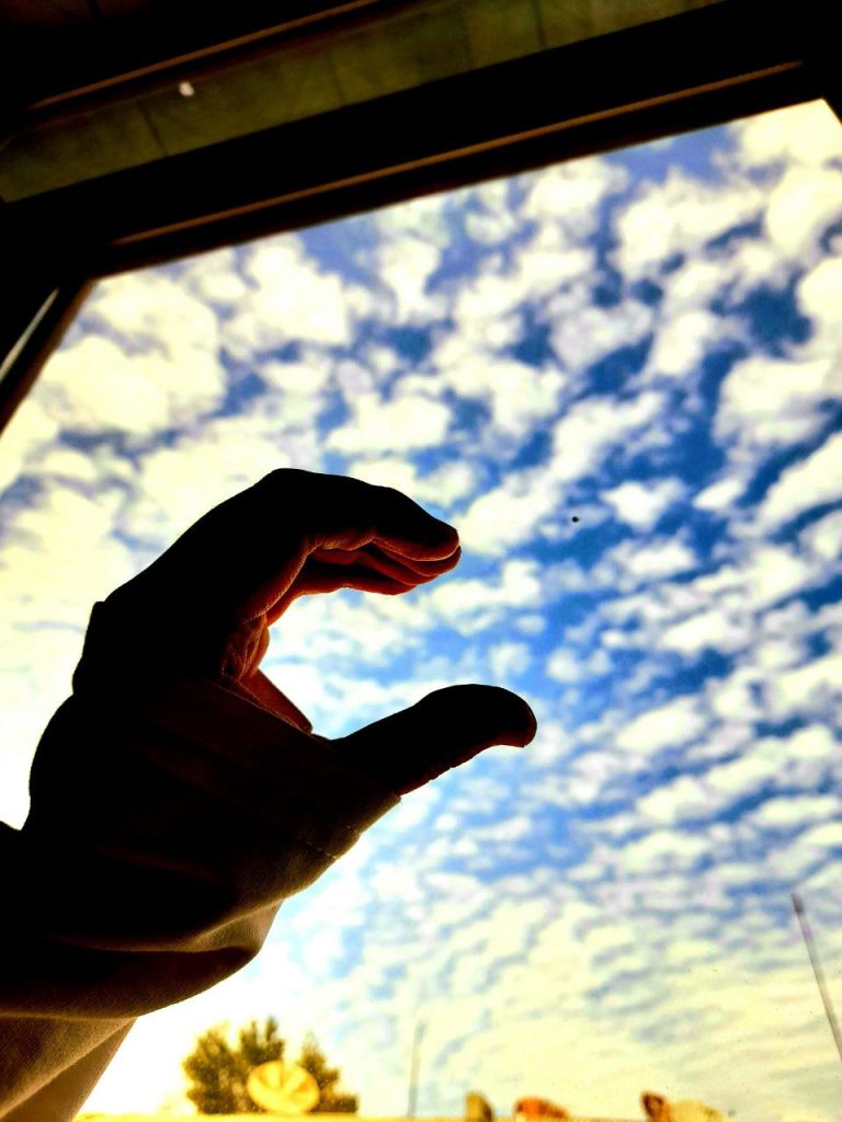 Outstretched open hand of a person of indeterminate race and gender reaching out to high cirrus clouds on a sunny day. 