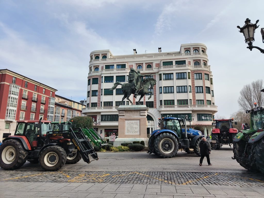 Several tractors parked in front of the statue of the figure with wings and a sword on a horse. 