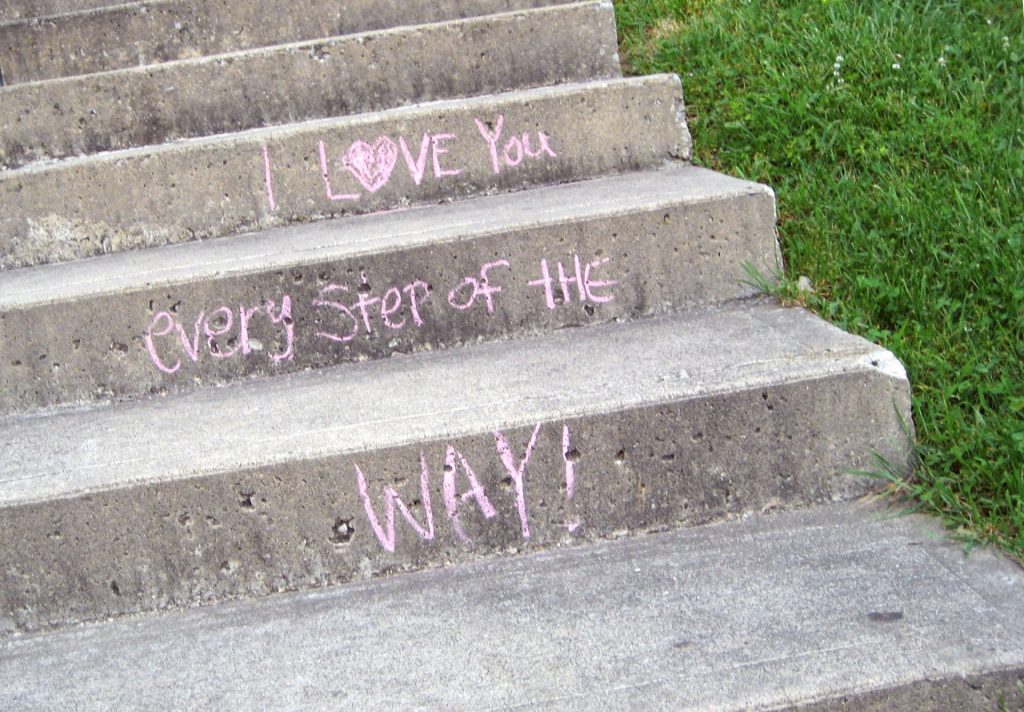 Concrete steps in a field of grass with pink chalk on each step reading, "I Love You Every Step of the Way!" 