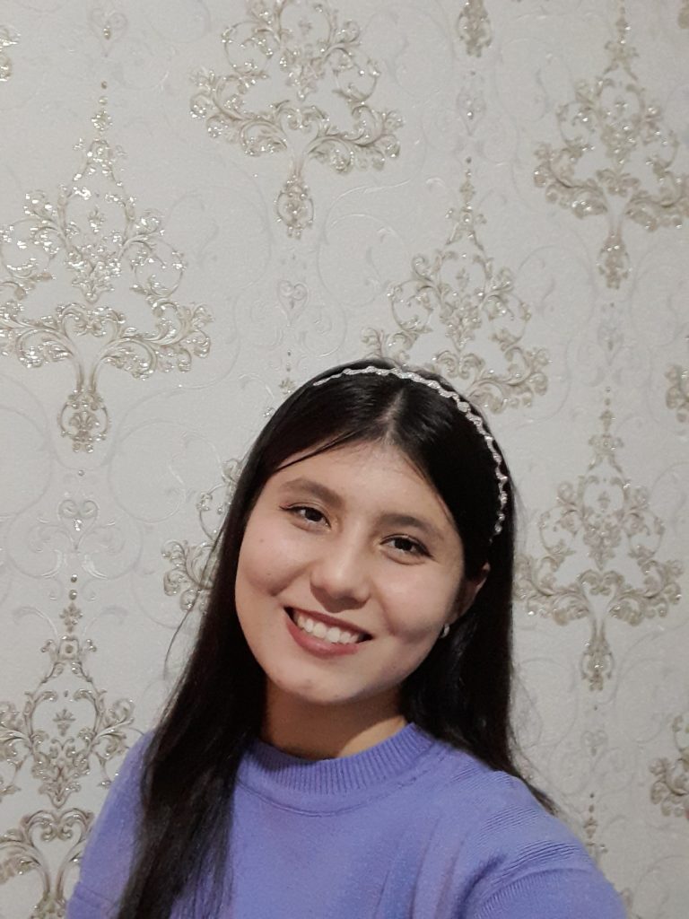 Central Asian teen girl with long dark straight hair and a headband and a smiling face and purple sweater. 