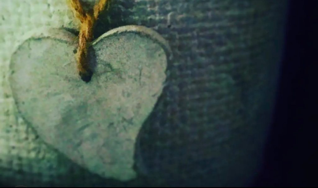 Carved metal heart tied to cloth with a brown string.