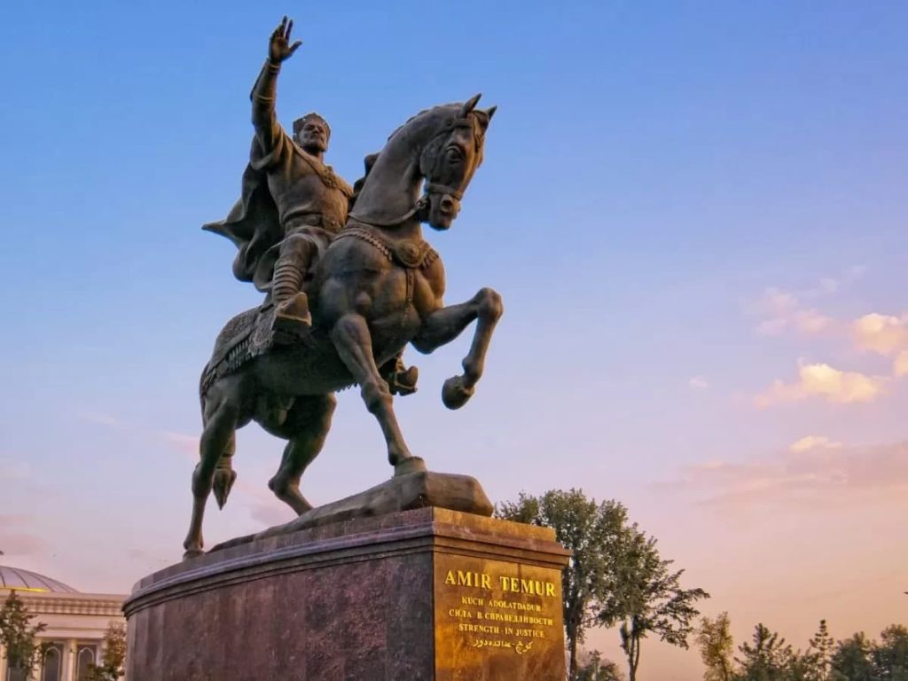 Statue of a man raising his arm on a running horse. Sunrise/sunset with blue sky and some clouds in the distance. 