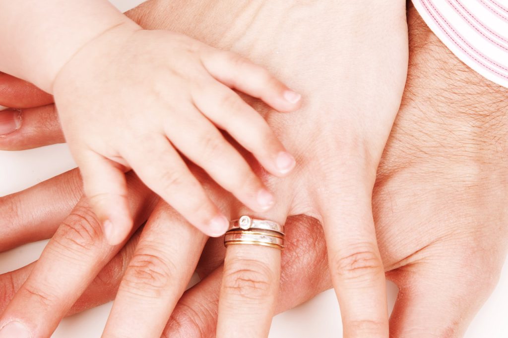 Mother, father, and baby's hands stacked on top of each other. Mom's wedding ring is visible and baby has tiny pudgy hands. 