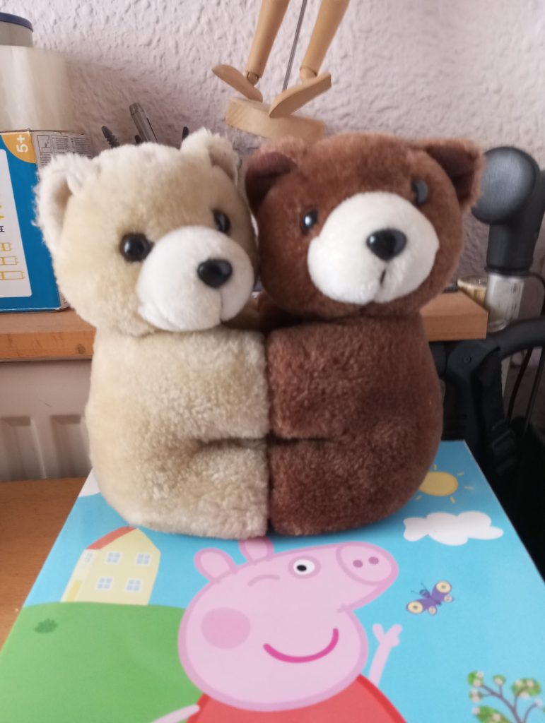 A white and a brown teddy bear embracing atop a Peppa Pig mat. 