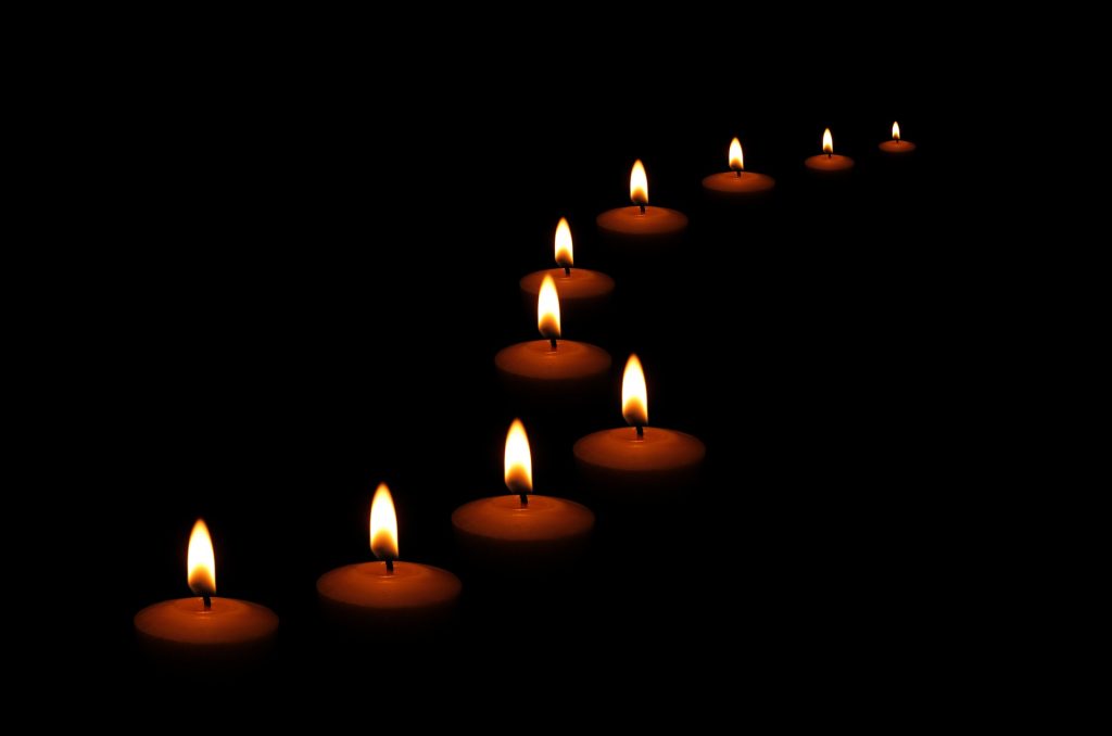 Winding row of lit candles in pitch black. 