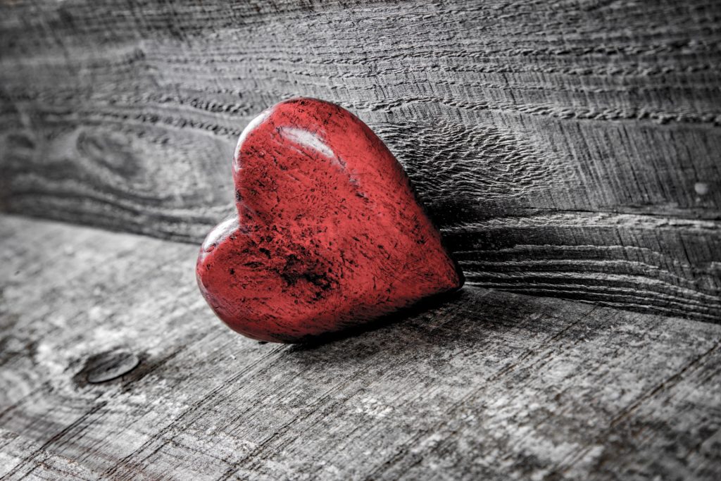 Red wooden heart with a shiny smooth surface up against gray wood. 
