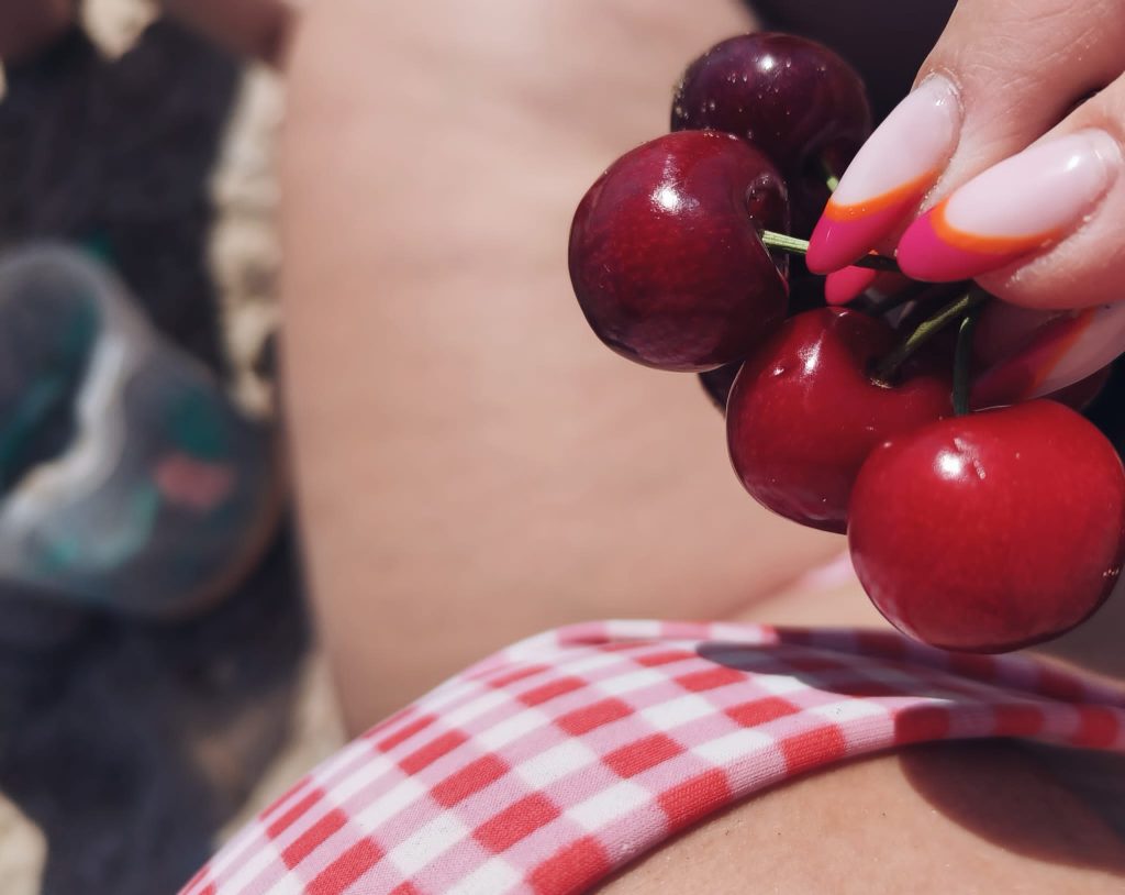 Someone's manicured hand holds a bunch of cherries over a white and red checkered towel. 
