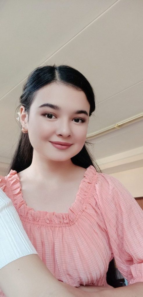 Central Asian teen girl with long straight dark hair, brown eyes, and a ruffly pink blouse. 