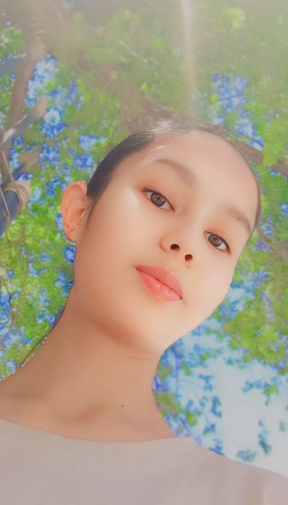 Teen Central Asian girl's headshot in front of a leafy tree canopy on a bright sunny day. 