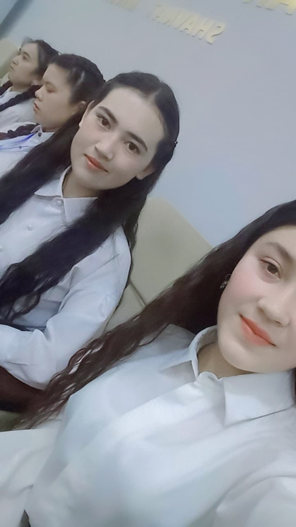 Central Asian teen girls in white collared school uniform shirts and long dark braided hair standing in a line next to each other. The author of this piece is in the middle facing the camera.