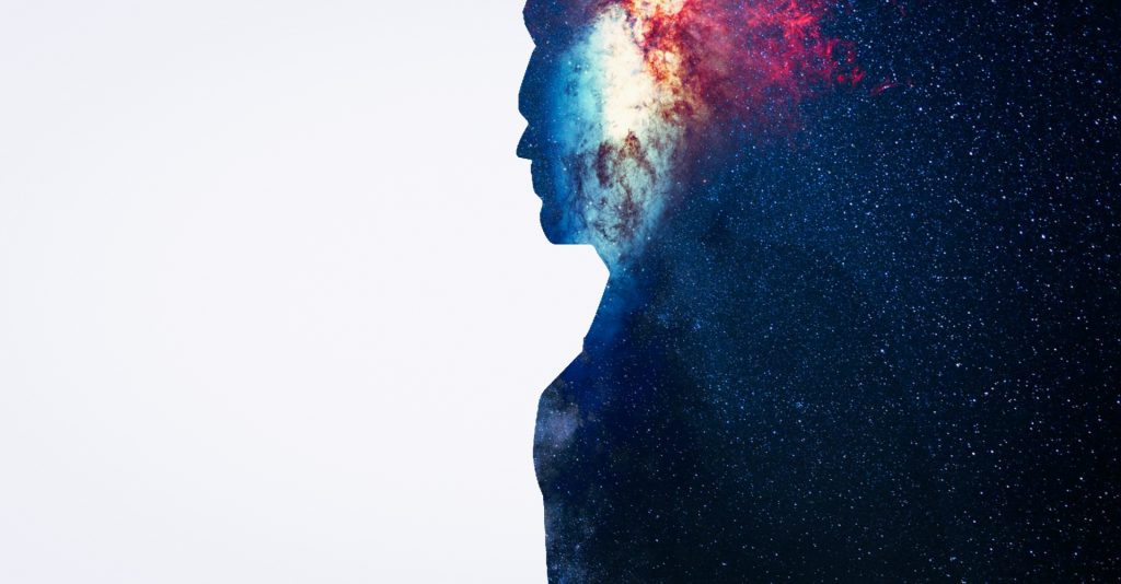Silhouette of a person in profile looking off to their left. Inside the silhouette are stars and a nebula. 