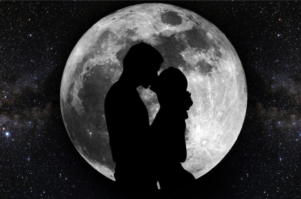 Silhouette of two lovers in front of the gray moon at night with stars and galaxies off in the distance. 