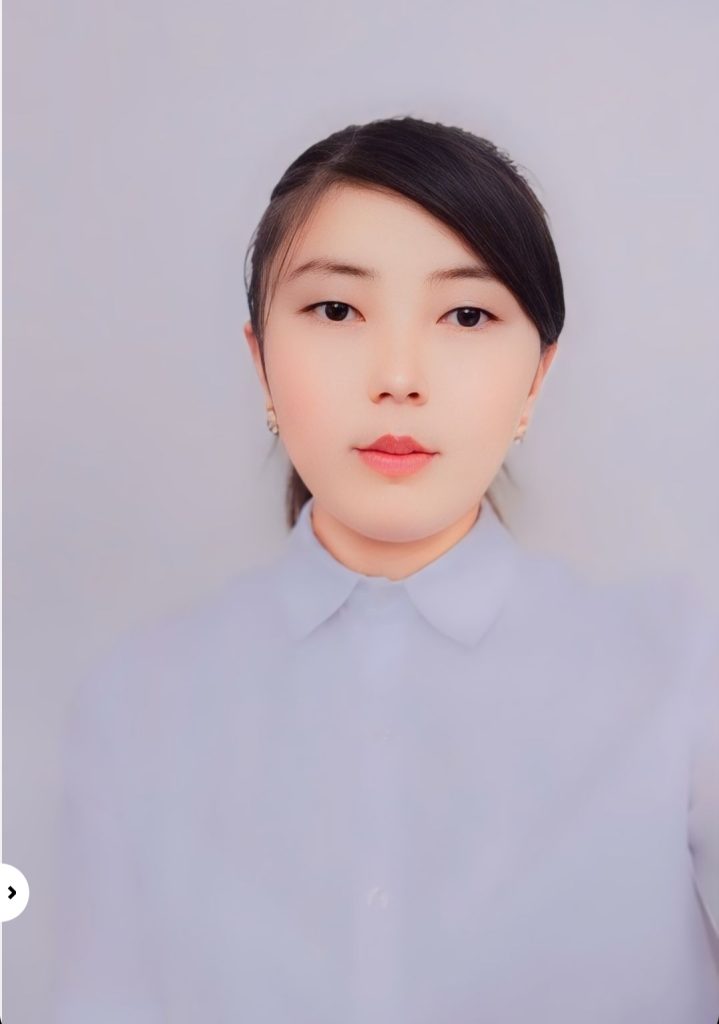 Young Central Asian woman with straight black hair behind her head, brown eyes, small earrings, and a gray collared shirt. 