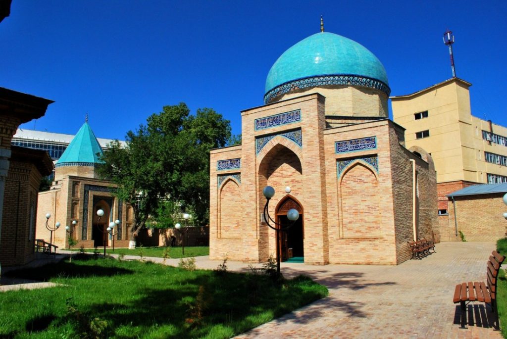 Large tan brick building with light blue onion domes. There's a green lawn and brick walkway. 