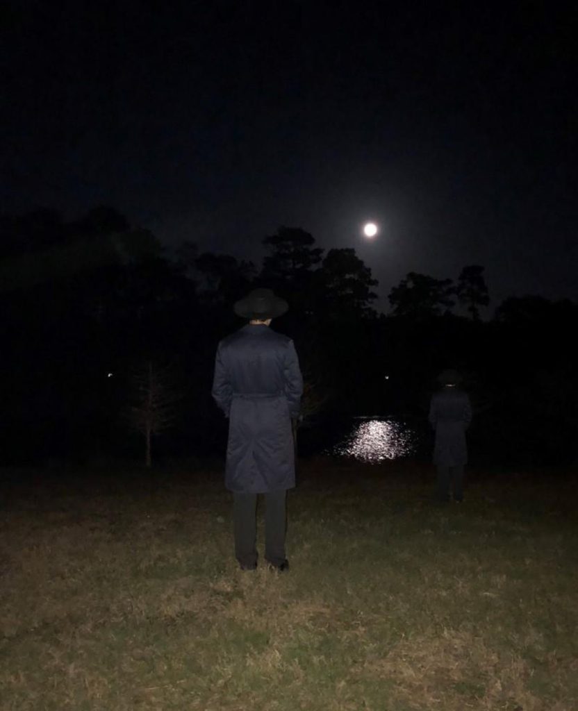 Realistic man in a coat and pants and black hat heading off into the moonlight near water. 