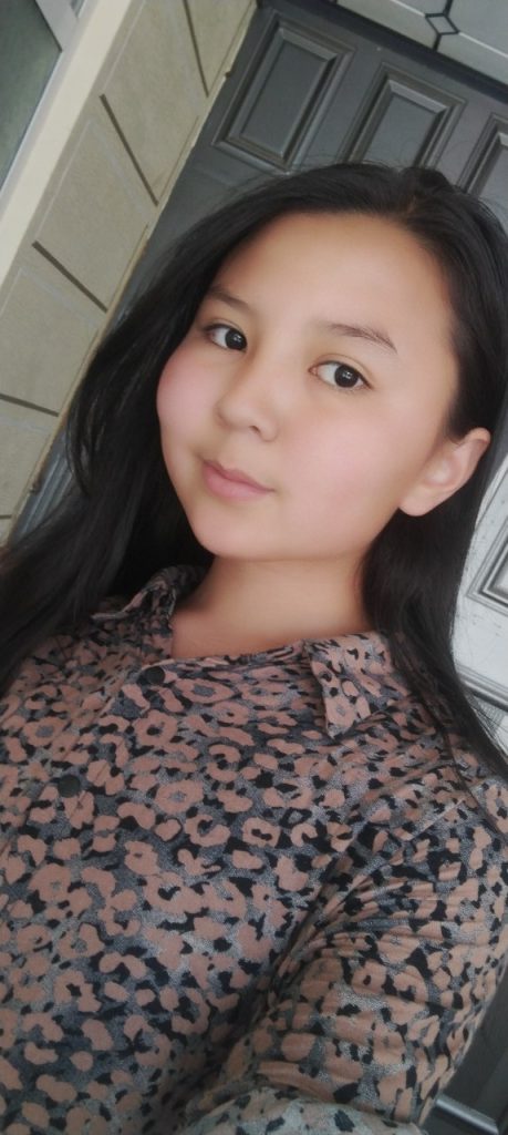 Central Asian teen girl with long dark hair, brown eyes, and a black, gray and pink floral top. 