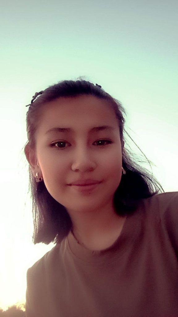 Central Asian teen girl with short dark hair, earrings, and a dark colored tee shirt. 