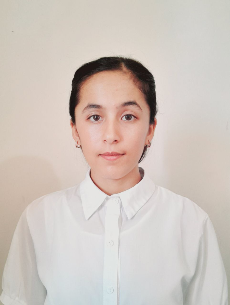 Young Central Asian woman with brown hair up in a bun, brown eyes, small earrings, and a white collared shirt. 