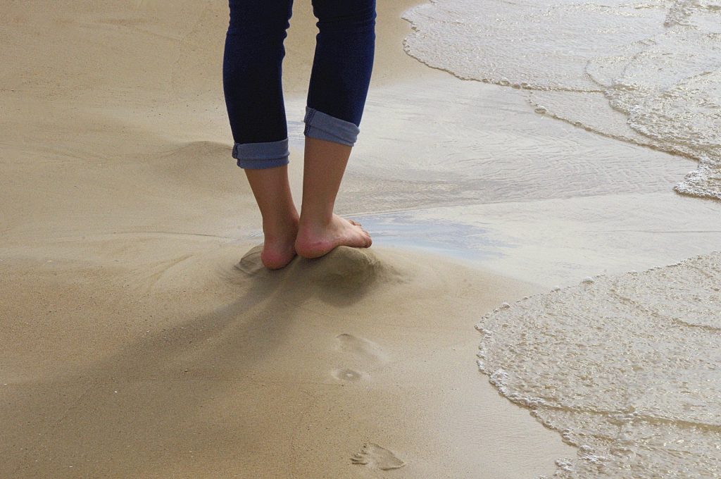 Person with rolled-up jeans leaving footprints in wet sand on the beach. 