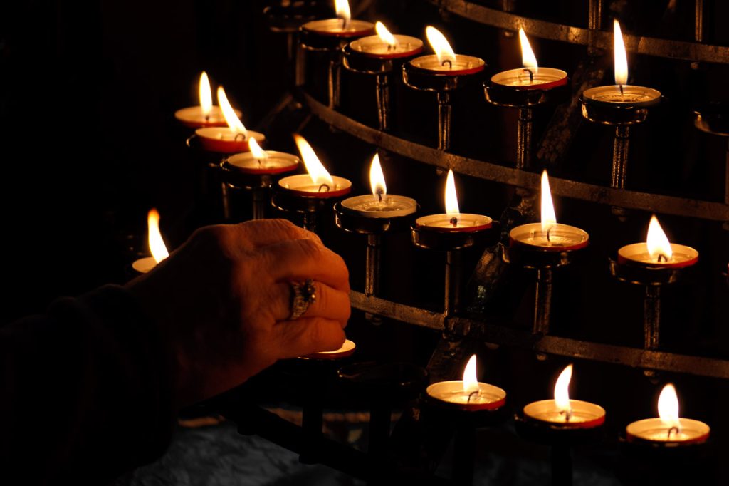 Woman's hand lighting candles in church in darkness. 