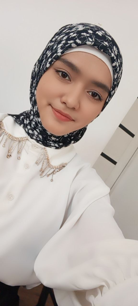 Teen Central Asian girl with a black and white headdress, brown eyes, and a white collared shirt with buttons and beads. 