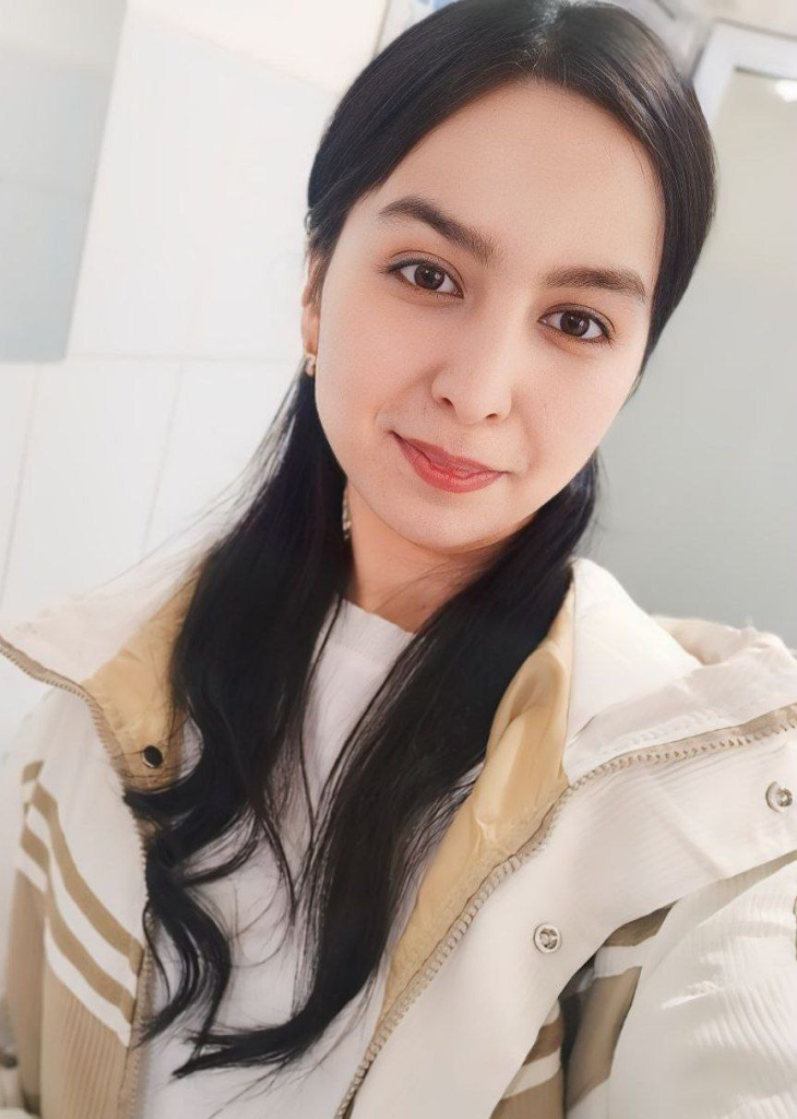 Central Asian teen girl headshot with dark hair, a brown coat, and gentle smile.