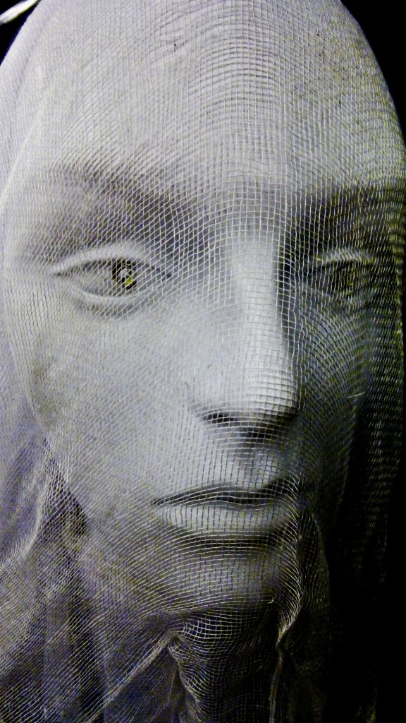 Thin fabric veil over a stone statue head of a woman with open eyes. Like a ghost bride.