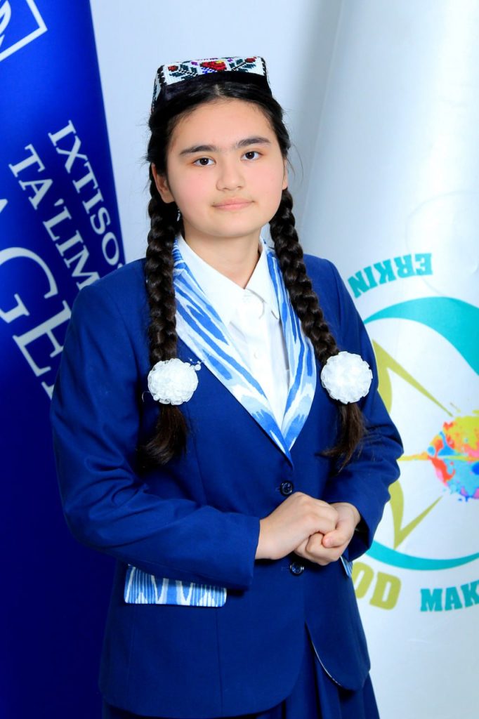 Central Asian teen girl with long dark braided hair, brown eyes, and an embroidered headdress standing in front of blue and white national flags.