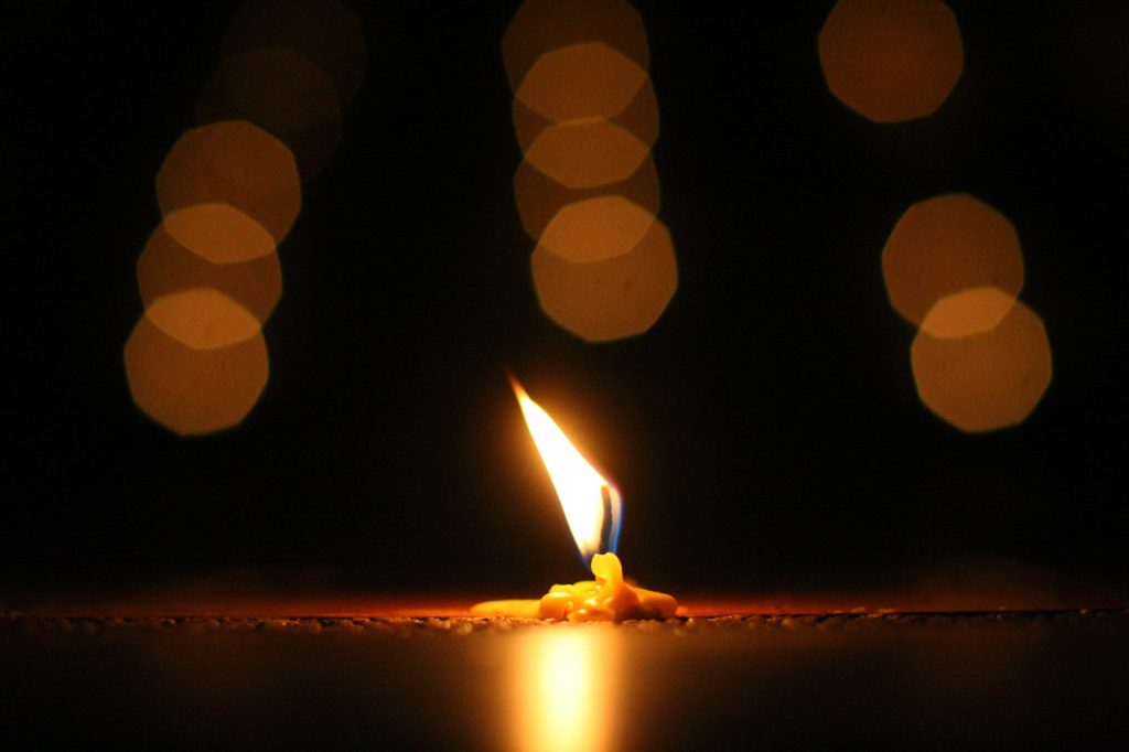 Single candle burning in darkness, bits of reflected light above the flame. 