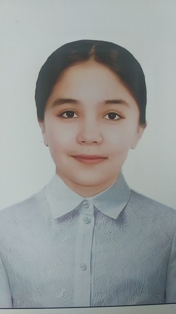 Young teen Central Asian girl with brown hair behind her head, brown eyes, and a white collared shirt. 