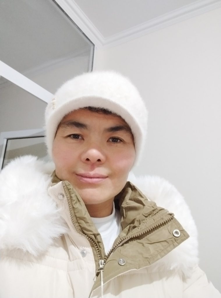 Central Asian woman in a knit winter hat and brown coat with white fur at the shoulders. Younger middle-aged. 