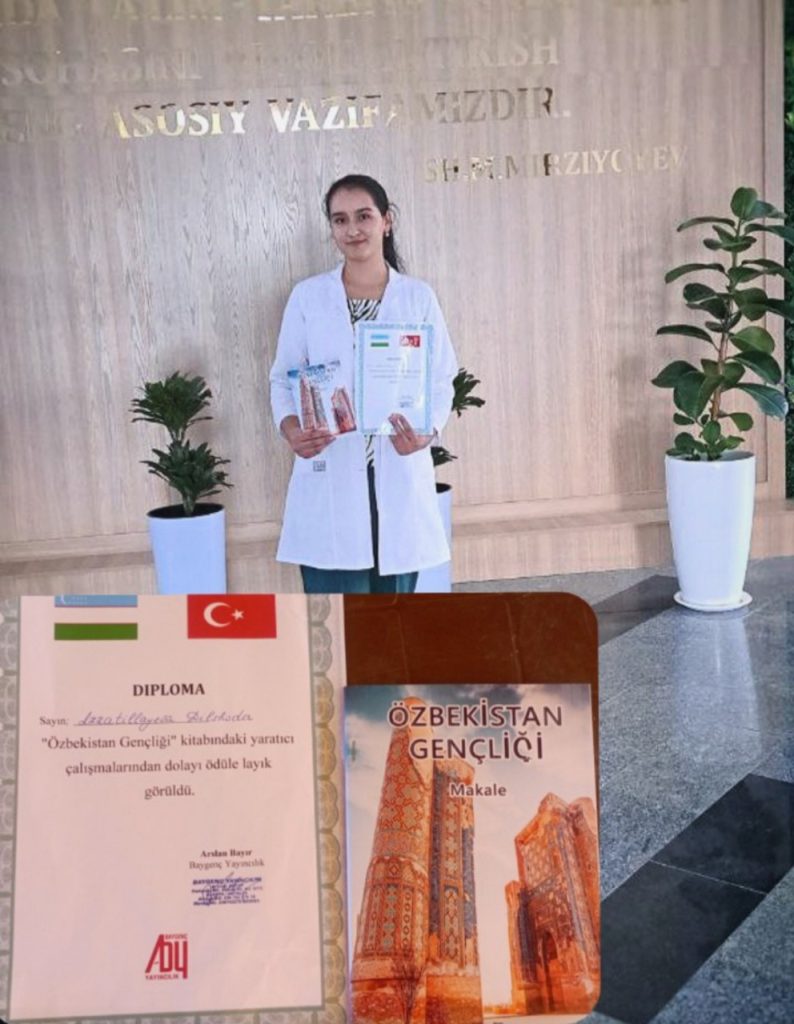 Young Central Asian woman with dark hair behind her head in a white coat holds up awards on a stage with some plants and a title. In front of her is a diploma from an Uzbek school. 