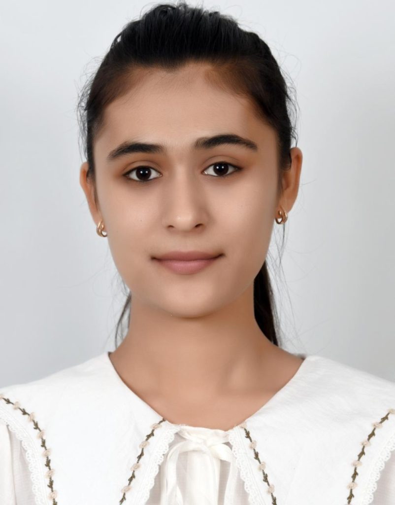 Headshot of a teen Central Asian girl with long dark hair behind her head, small earrings, brown eyes, and a white ruffled blouse. 