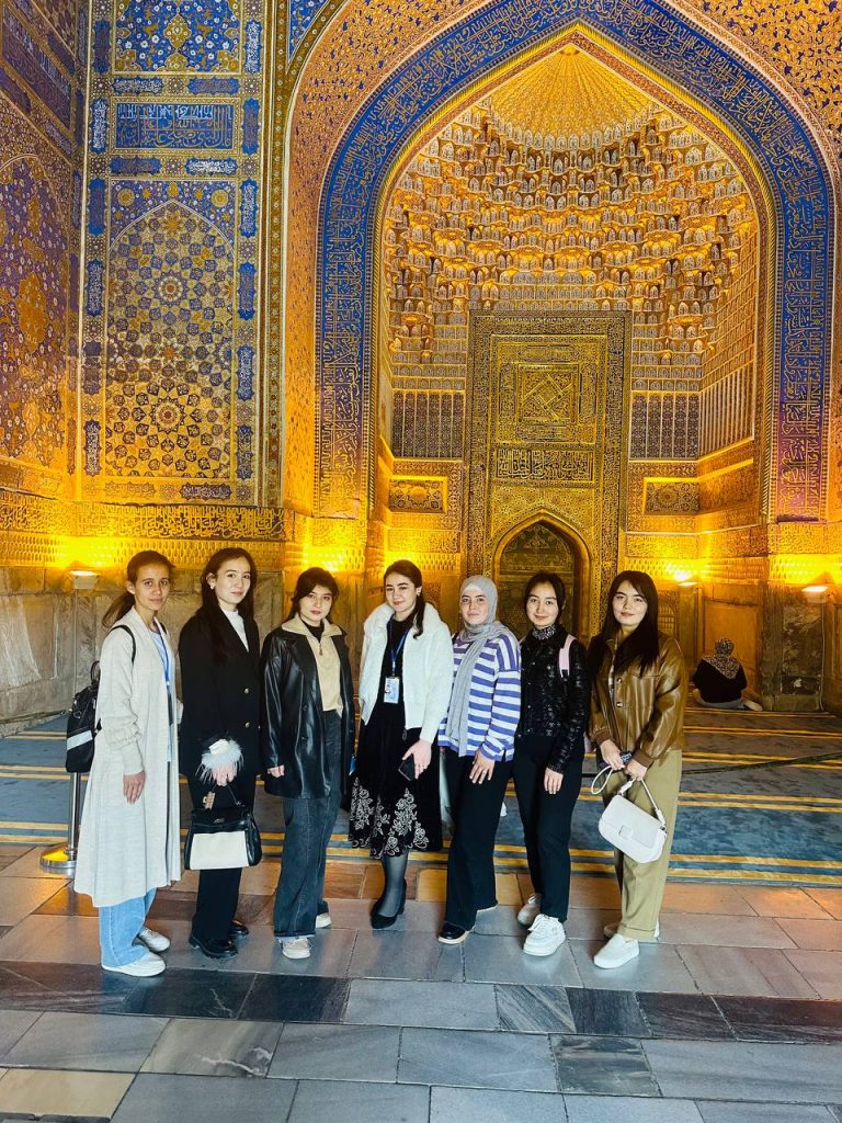 Smaller group of young women students inside an intricately decorated blue and gold building.