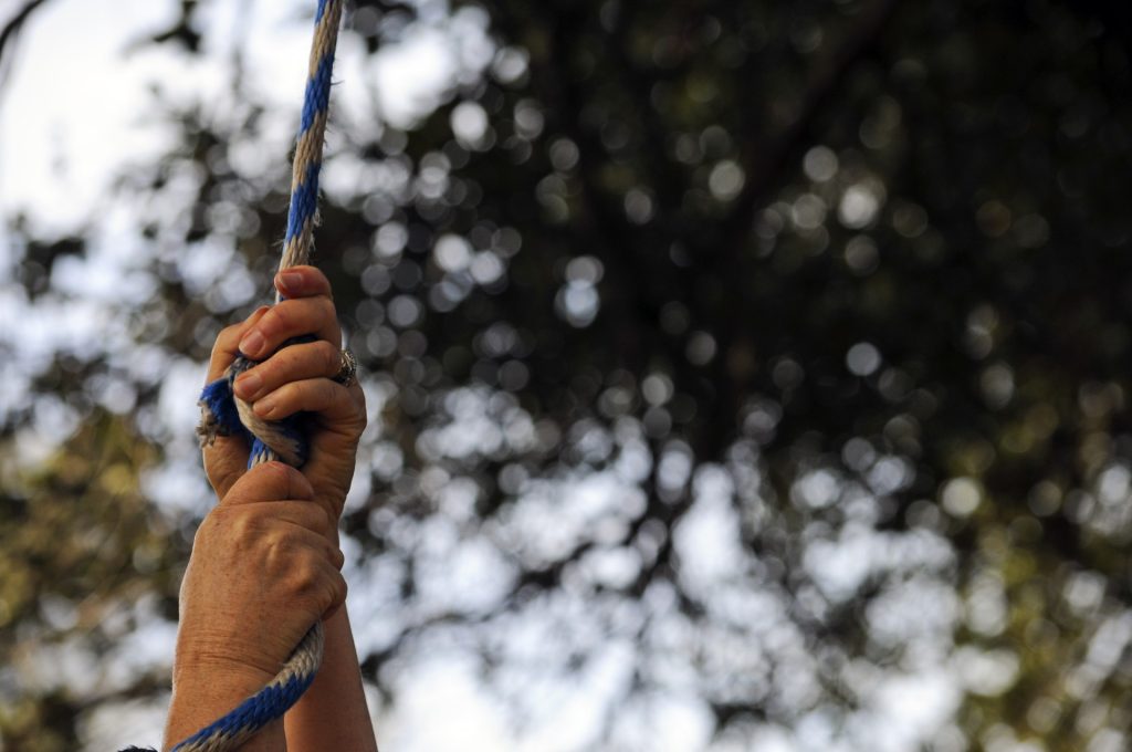 Person's hand gripping a rope with trees in the background. 