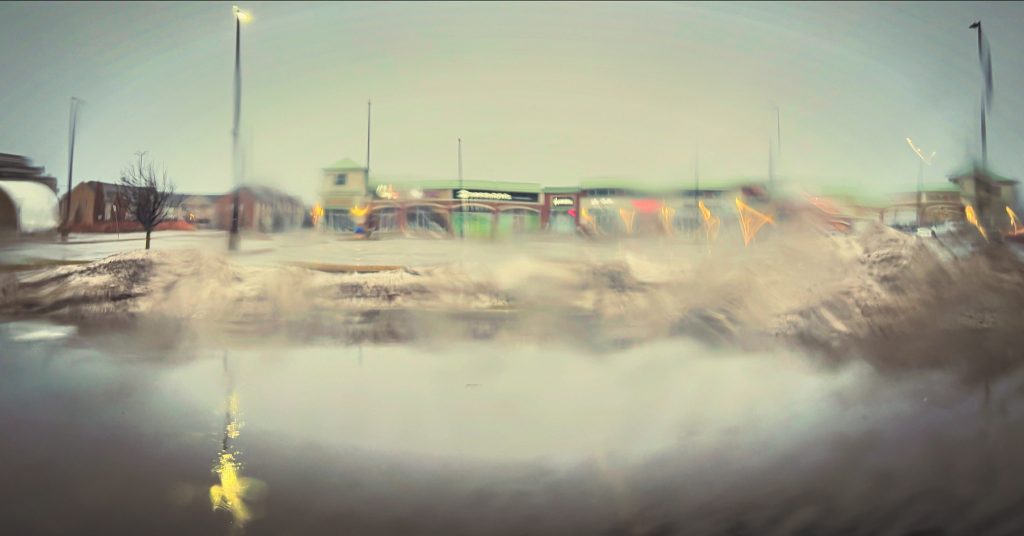 Hazy image of a town with some brick buildings, a frozen lake, and snow dusting brown dirt. 