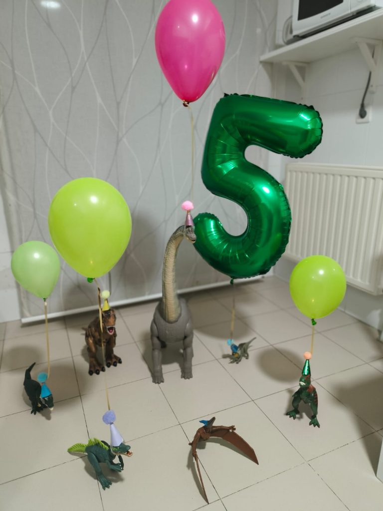 Green number 5 balloon, green and yellow balloons attached to various dinosaur action figures. 