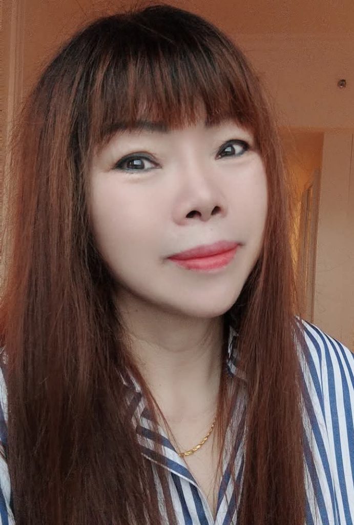 East Asian woman with longer straight brown hair, brown eyes, and a white and gray striped collared shirt and small thin necklace. 