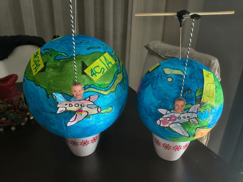 Two globes with drawings of airplanes and a boy's face suspended from sticks and string on a table. 