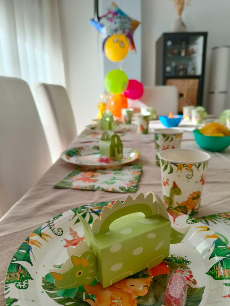 Table set for a child's birthday, paper plates and dinosaur napkins and paper cups, and balloons. 