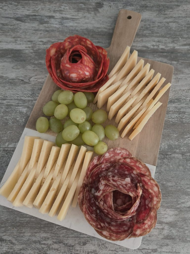 Snack board, green grapes, salami rosettes, slices of white cheese. 