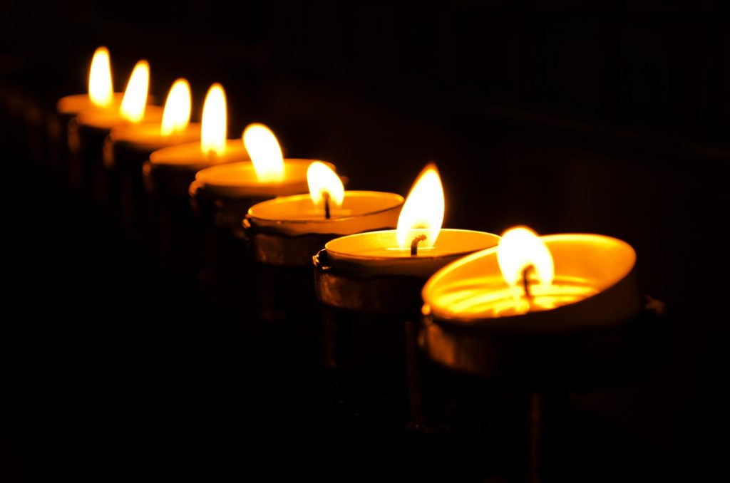 Row of candles burning in pitch black darkness.