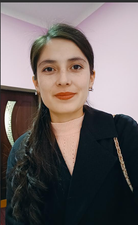 Young woman with long dark hair, a black coat, and a pink sweater.
