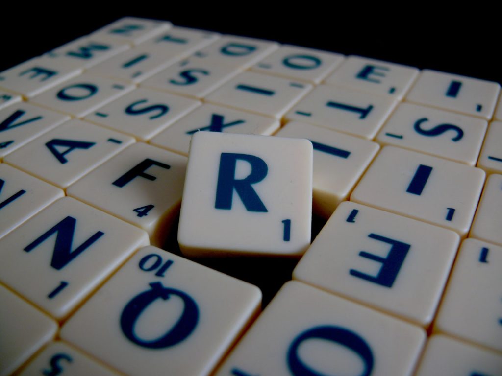 Scrabble tiles, blue text on white tile. The R, worth one point, is jostled out of place in the middle.