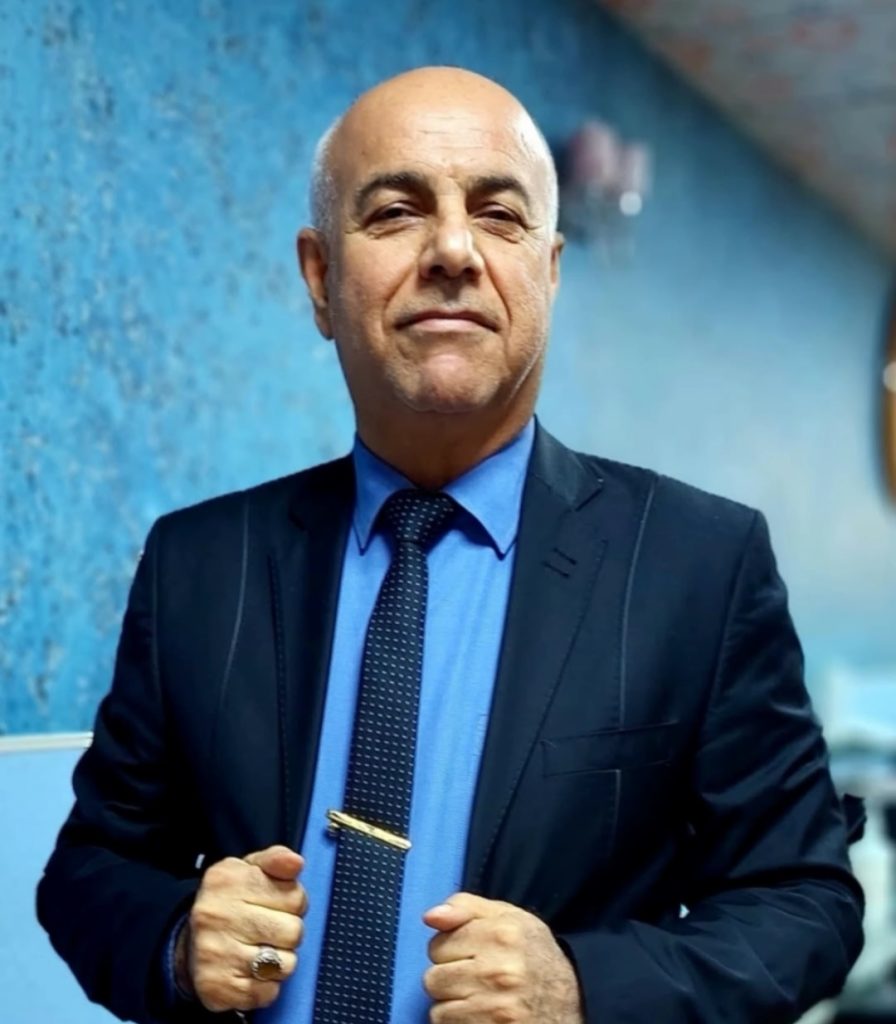 Older bald man of Arab heritage in a black and blue suit.