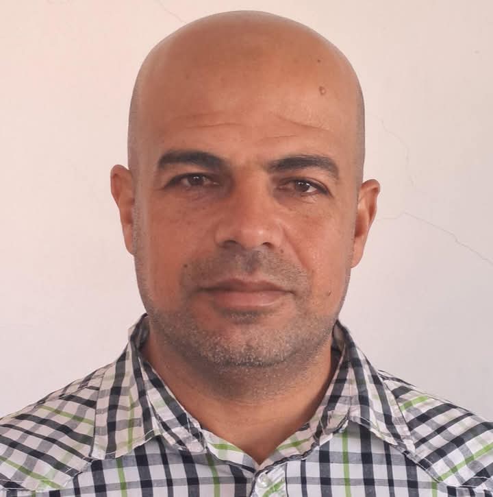 Middle aged bald man of Arab heritage in a green and black and white plaid shirt.